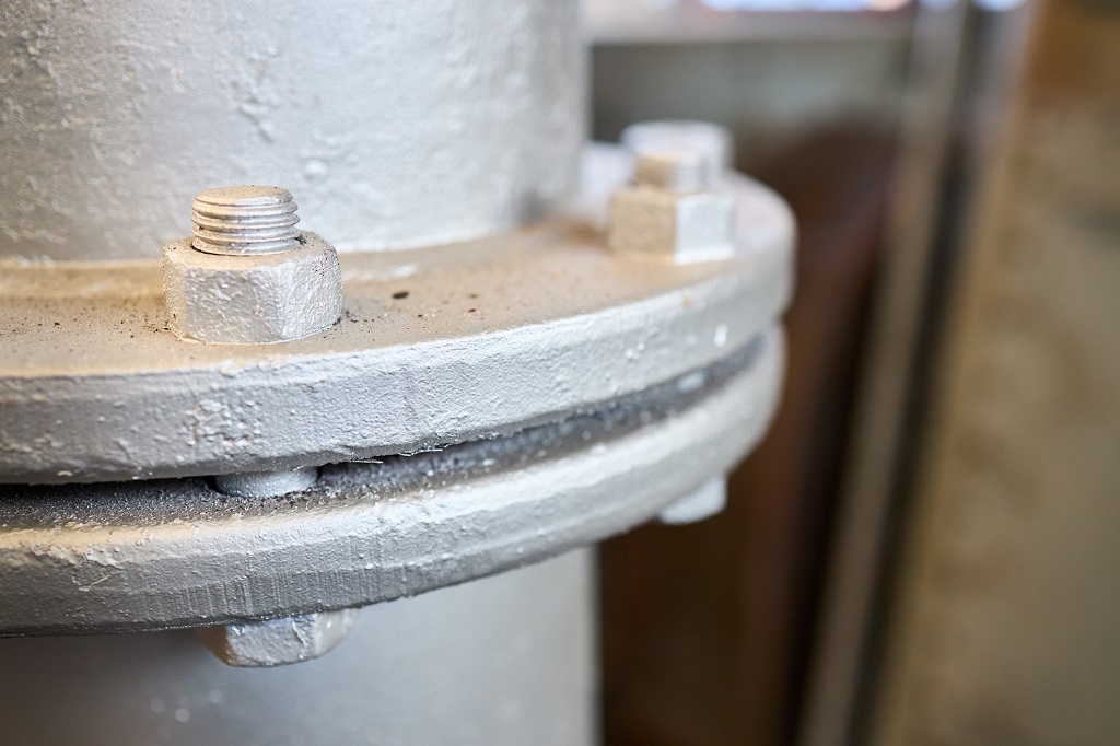 Bolted screw flenged connection, sealing connection on manhole of industrial machine compressor or pump on chemical plant selective focus with out of focus industrial background with copyspace.